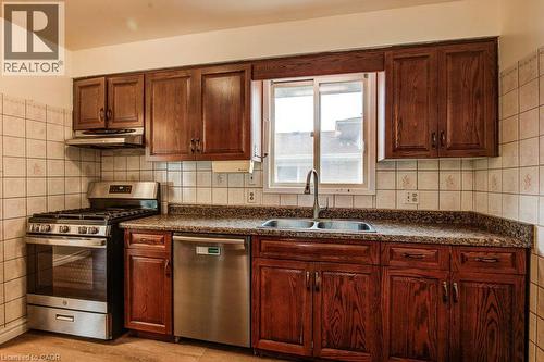 Wood-finish cabinetry, stainless steel gas range, stainless steel dishwasher, double basin sink, and tile backsplash - 143 Sunrise Place, Kitchener, ON 