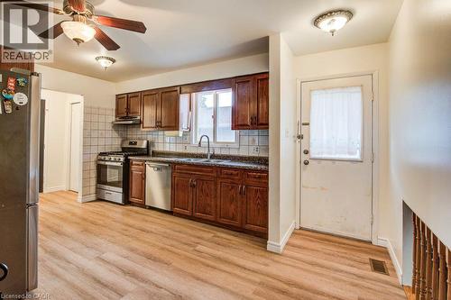 Kitchen with wood-finish flooring, dark wood cabinetry, a tile backsplash, and stainless steel appliances - 143 Sunrise Place, Kitchener, ON 