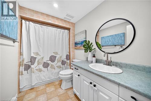 White vanity with black cabinet hardware, oval undermount sink, and a circular black-framed mirror - 1517 Elm Road Unit# 9, Oakville, ON 