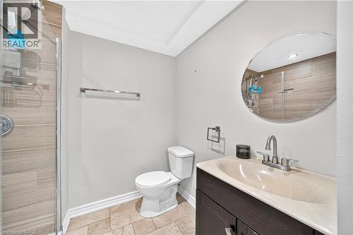 Enclosed shower with horizontal tile-finish walls, a dark wood-finish vanity with an integrated sink, a circular wall mirror, and a toilet - 1517 Elm Road Unit# 9, Oakville, ON 