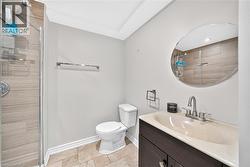 Enclosed shower with horizontal tile-finish walls, a dark wood-finish vanity with an integrated sink, a circular wall mirror, and a toilet - 