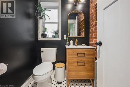 Bathroom featuring a wood-finish vanity with drawer storage, a white ceramic sink, a patterned tile floor, and an exposed brick accent wall - 58 Balmoral Avenue N, Hamilton, ON 