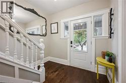Hardwood flooring, white paneled entry door with glass inserts, white framed sidelight windows, and white painted staircase with balusters - 