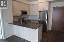 Kitchen featuring a peninsula, appliances with stainless steel finishes, dark wood-style flooring, and dark stone countertops - 1105 Leger Way Unit# 329, Milton, ON 