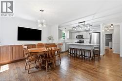 Open-concept kitchen and dining area featuring wood-finish flooring, a kitchen island with seating, stainless steel appliances, and updated light fixtures - 