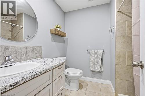 Bathroom featuring a white vanity with a patterned countertop, circular mirror, and tile flooring - 72 Crestlynn Crescent, Simcoe, ON 