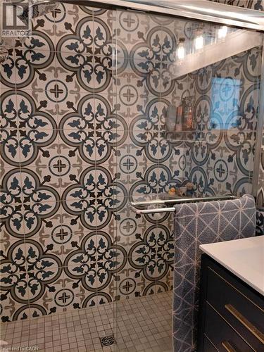 Patterned wall tile in a shower enclosure with a glass door, integrated shower niche, and mosaic tile floor - 244 Guildwood Drive, Hamilton, ON 