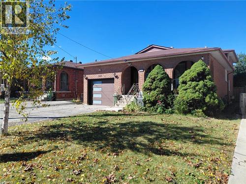 Brick exterior with arched window openings, a contemporary garage door, and a front yard with established plantings - 244 Guildwood Drive, Hamilton, ON 