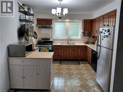 Kitchen featuring wood-finish cabinetry, patterned floor tiles, white tile backsplash, and a window with frosted glass details - 244 Guildwood Drive, Hamilton, ON 