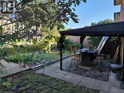 Paved patio area featuring a fixed overhead cover, wood decking, and planted garden beds - 