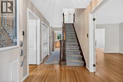 Entryway featuring wood-finish flooring, a carpeted staircase with wood banister, and a paneled front door with decorative glass - 