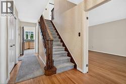 Wood-finish flooring throughout, carpeted staircase with wood banister, and a separate room with light-toned walls - 