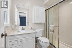 Bathroom featuring a white vanity with a light-colored countertop, an undermount sink, a wall-mounted mirror, a toilet, and a glass-enclosed shower - 