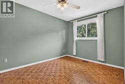 Parquet wood-finish flooring, light green wall paint, overhead ceiling fan with lighting, white trim, and a window with white casing - 