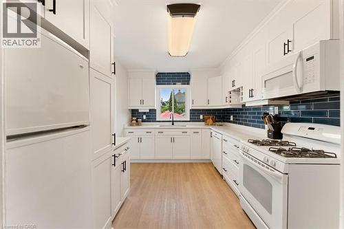 Kitchen featuring white cabinetry with black hardware, wood-finish flooring, white countertops, a blue subway tile backsplash, and a window above the sink - 17 Craigmiller Avenue, Hamilton, ON 