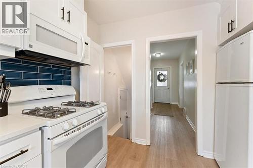 Kitchen featuring white cabinetry with dark hardware, a white range with an above-range microwave, white refrigerator, and a blue subway tile backsplash - 17 Craigmiller Avenue, Hamilton, ON 