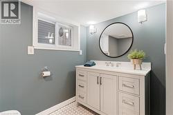 Bathroom featuring a white vanity with brushed nickel hardware, white countertop, and a circular black-framed mirror - 