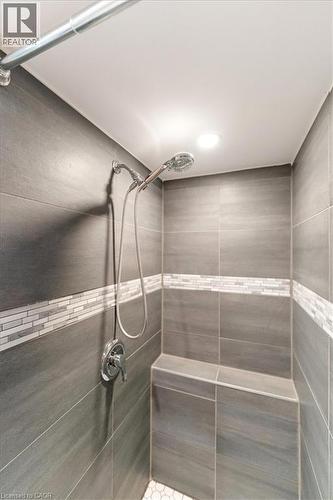Shower stall featuring large format gray wall tiling, a decorative mosaic tile accent band, a built-in bench, a handheld showerhead, and recessed ceiling lighting - 17 Craigmiller Avenue, Hamilton, ON 