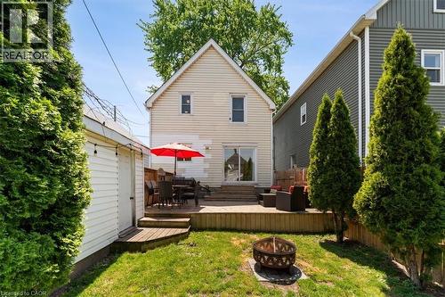 Spacious backyard featuring a wooden deck, sliding glass door access to the residence, a dedicated fire pit area, a detached garage with horizontal siding, and mature evergreen trees lining the proper - 17 Craigmiller Avenue, Hamilton, ON 