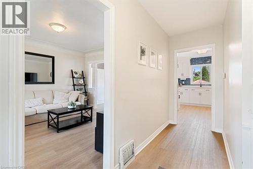 Hallway with wood-finish flooring leading to a kitchen featuring white cabinetry, a dark blue subway tile backsplash, and a window with outdoor greenery - 17 Craigmiller Avenue, Hamilton, ON 