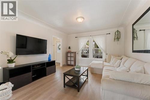 Living area with wood-finish flooring, crown molding, and a window featuring white curtains - 17 Craigmiller Avenue, Hamilton, ON 