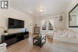Living area with wood-finish flooring, crown molding, and a window featuring white curtains - 