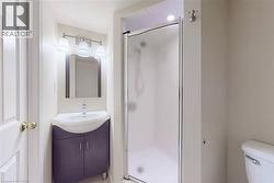 Bathroom featuring a corner vanity with integrated sink, framed mirror, three-light vanity fixture, and a glass-enclosed shower - 