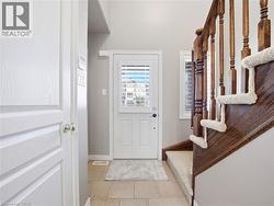 Front entry featuring neutral tile flooring, a white door with louvered glass, and a natural wood staircase with carpeted treads - 