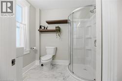 Curved glass shower enclosure, white shower surround, floating wood shelves, white toilet, and patterned floor tile - 