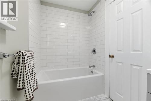 White subway tile shower surround, chrome shower and tub fixtures, white paneled door, and marble-look flooring - 87 Strathcona Avenue, Brantford, ON 