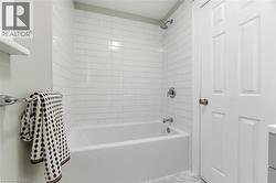 White subway tile shower surround, chrome shower and tub fixtures, white paneled door, and marble-look flooring - 