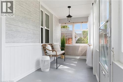 Enclosed porch with wide plank flooring, beadboard wainscoting, and a hanging light fixture - 87 Strathcona Avenue, Brantford, ON 