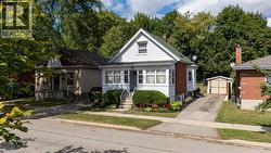 White siding exterior with brick accents, prominent front porch, mature landscaping, paved driveway, and detached garage - 