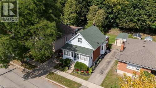 White siding exterior with brick accents, green shingle roof, and a mature tree canopy - 87 Strathcona Avenue, Brantford, ON 