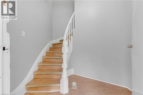 Curved wooden staircase featuring white balusters and a substantial newel post - 211 Wentworth Street N, Hamilton, ON 