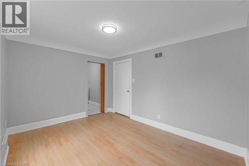 Light wood-finish flooring, light gray wall paint, flush mount ceiling light fixture, white trim, and a white interior door - 211 Wentworth Street N, Hamilton, ON 