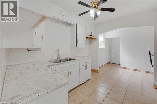 White cabinetry with brass hardware, dual basin stainless steel sink, patterned countertop, ceramic tile backsplash, and ceramic tile flooring - 211 Wentworth Street N, Hamilton, ON 