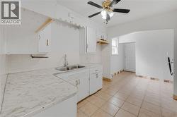 White cabinetry with brass hardware, dual basin stainless steel sink, patterned countertop, ceramic tile backsplash, and ceramic tile flooring - 