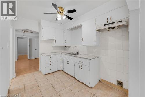 Kitchen featuring white cabinetry, a dual basin sink, light-toned tile flooring, and a ceiling fan - 211 Wentworth Street N, Hamilton, ON 
