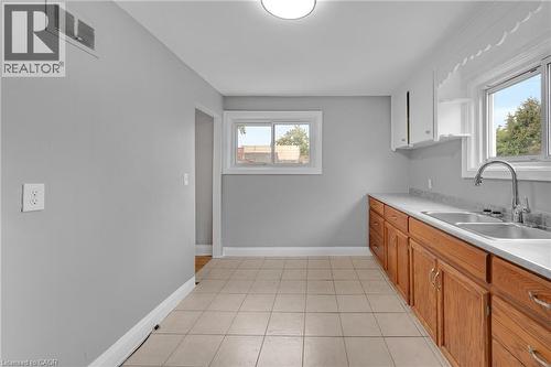 Kitchen featuring wood cabinetry, a dual basin stainless steel sink, a modern pull-down faucet, and tile flooring - 211 Wentworth Street N, Hamilton, ON 