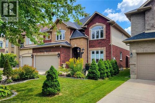 Red brick and stone facade with arched windows, multiple attached garages, and a manicured front lawn - 214 Cloverleaf Drive, Ancaster, ON 