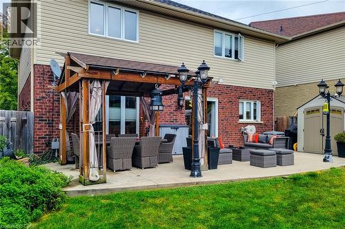 Expansive concrete patio featuring a wood pergola, brick exterior, and manicured lawn - 214 Cloverleaf Drive, Ancaster, ON 