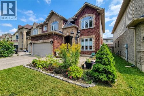 Brick and stone facade with arched windows, an integrated garage, and a landscaped front garden - 214 Cloverleaf Drive, Ancaster, ON 
