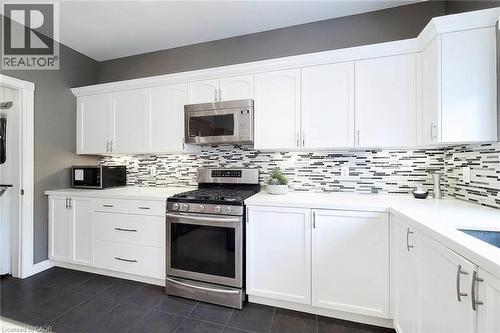 White cabinetry with crown molding, stainless steel appliances, solid surface countertops, mosaic tile backsplash, and dark tile flooring - 214 Cloverleaf Drive, Ancaster, ON 