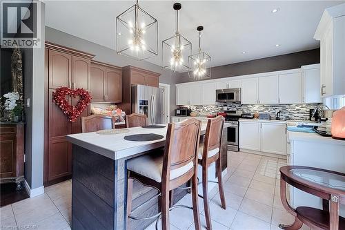 Kitchen featuring a multi-tone cabinetry design, central island with a light-toned countertop, stainless steel appliances, and a mosaic tile backsplash - 214 Cloverleaf Drive, Ancaster, ON 