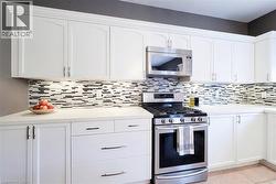 White cabinetry, stainless steel range and microwave, light-toned countertops, and a mosaic tile backsplash - 