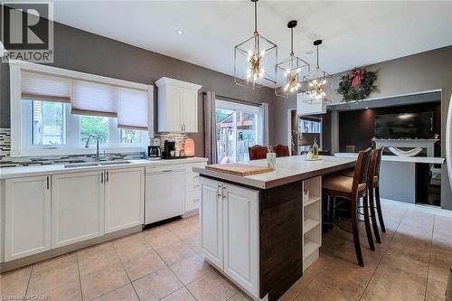 Kitchen featuring a center island with seating, white cabinetry, integrated dishwasher, and tile flooring - 214 Cloverleaf Drive, Ancaster, ON 