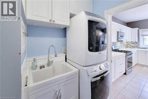 Utility sink with chrome faucet, upper and lower cabinetry, stackable washer and dryer, and tiled flooring - 214 Cloverleaf Drive, Ancaster, ON 