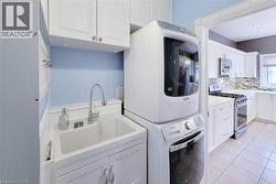 Utility sink with chrome faucet, upper and lower cabinetry, stackable washer and dryer, and tiled flooring - 