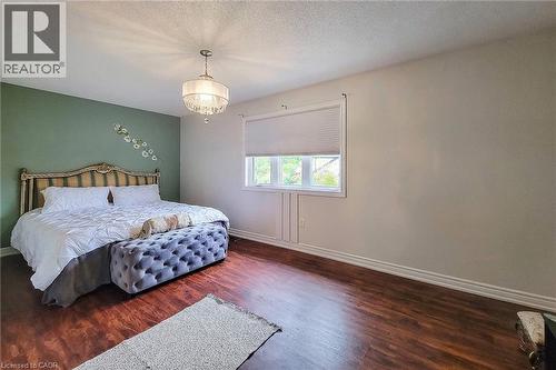Wood-finish flooring, single window with blinds, decorative light fixture, painted accent wall, and white trim - 214 Cloverleaf Drive, Ancaster, ON 